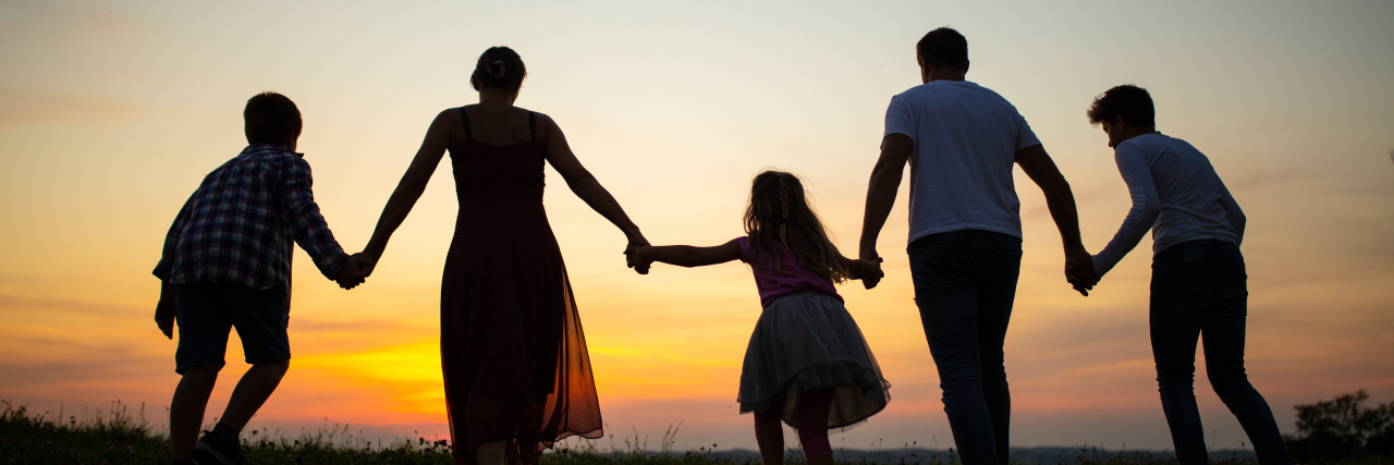 Family holding hands and walking together at sunset.