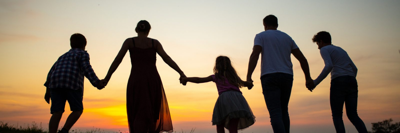 Family holding hands and walking together at sunset.
