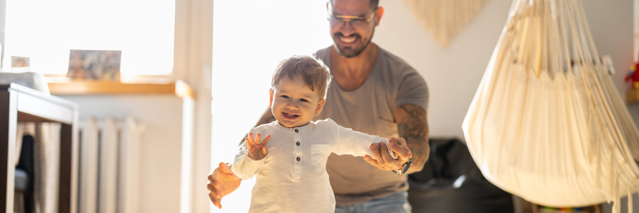 Navigating Being a Parent With a Disability in Parent/Child Programs Happy father helping toddler walk.