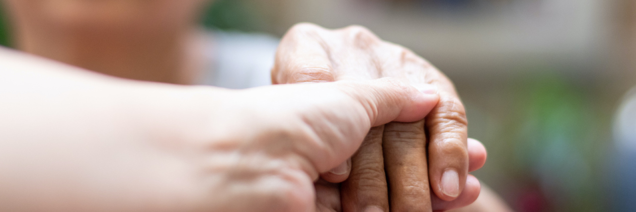 Reflections on Caregiving For a Parent Close-up of a caregiver holding the hand of an older adult in a comforting gesture.