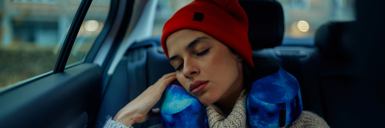 Woman with neck pillow sleeping in car while traveling on road trip.