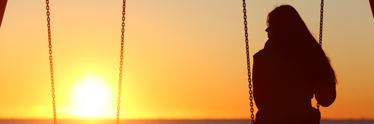 Woman on a swing at sunset on the beach, looking at the empty swing next to her