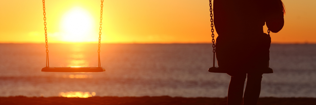 Woman on a swing at sunset on the beach, looking at the empty swing next to her