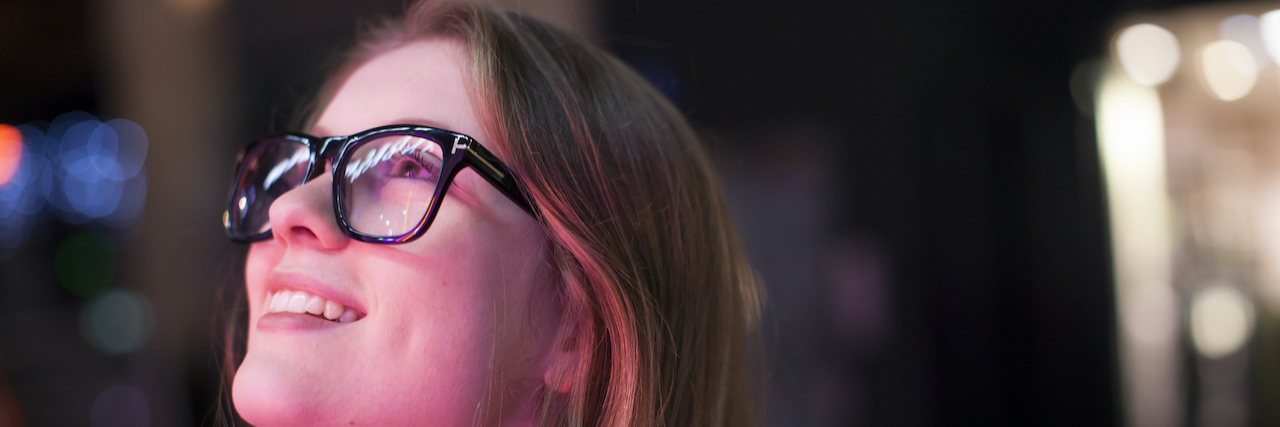 Woman wearing glasses looking up at lights at night