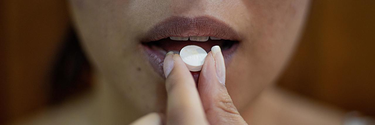photo of a woman raising medication in pill form to her lips