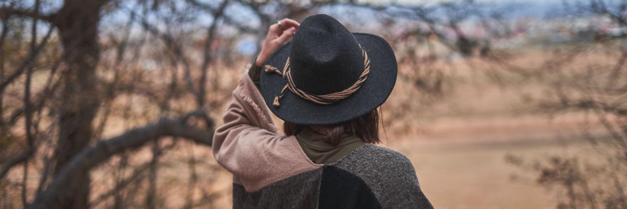 My Battle With Depression and Grief After My Cousin Died by Suicide Back of a woman with a sweater and hat, walking outside during the fall