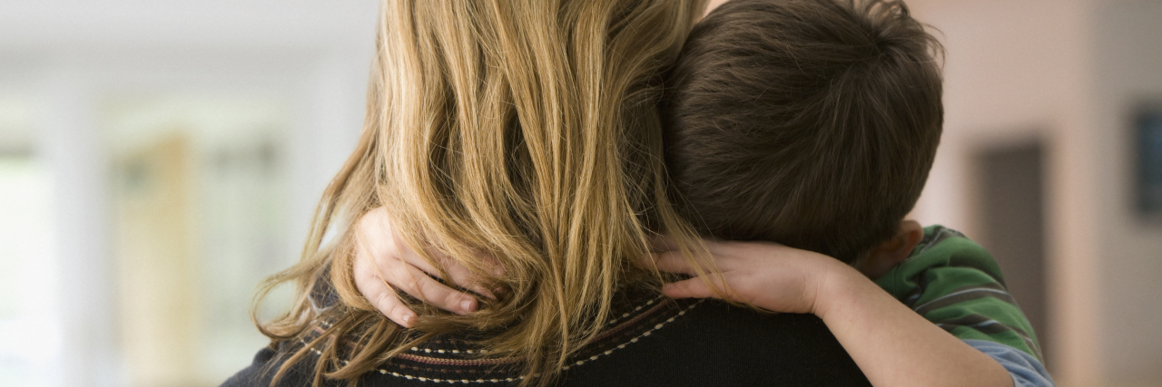 Staying at the Ronald McDonald House as a Parent Photo from behind of a blonde woman in a black sweater holding a white, brunette young boy whose arms are wrapped around her and whose head is rested on her shoulder.