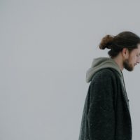 Man with his hair in a bun walking in the snow looking down