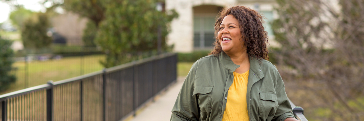 Black woman outside on paved path looking to the side and smiling