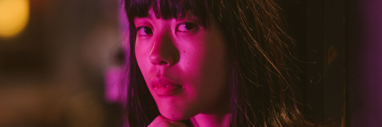 My Struggle to Accept Myself as an Autistic Woman A portrait of a young woman lit up by neon lights at night.