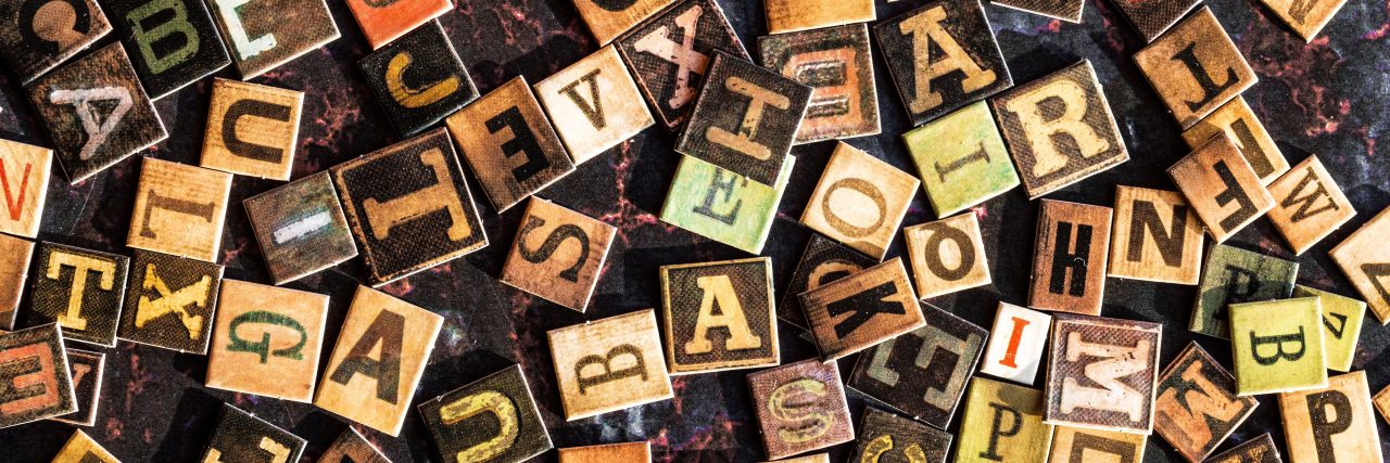 Feeling Reduced to Acronyms in Life With Chronic Illness Colored alphabet tiles scattered across rusted metal surface