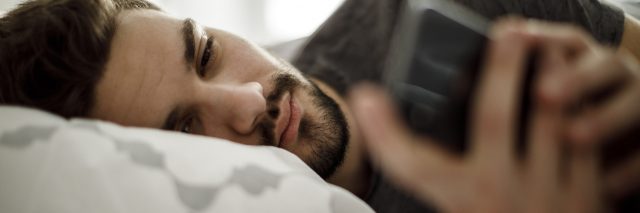 Man lying in bed on his side, looking at his phone