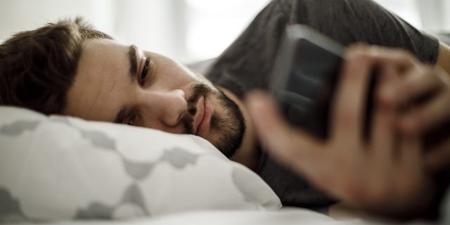 Man lying in bed on his side, looking at his phone