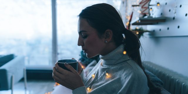 Photo of a woman drinking hot chocolate in the living room of her apartment; enjoying the peaceful winter morning.