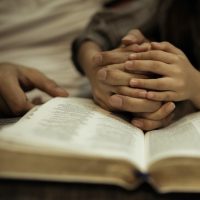 Child's hands intertwined with adults fingers above the Bible