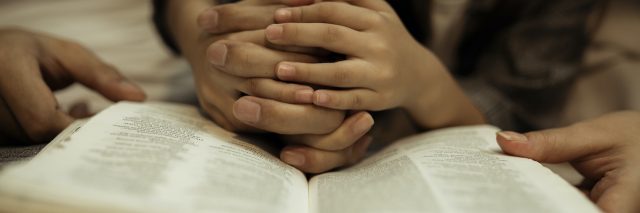 Child's hands intertwined with adults fingers above the Bible