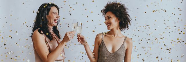 Two women dressed up clinking glasses of champagne, smiling