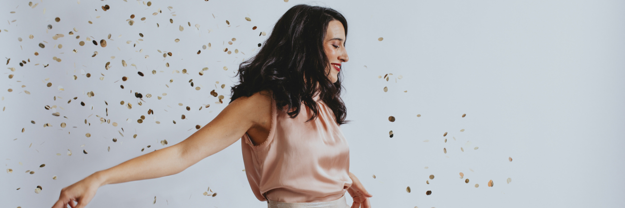 Reflecting on 2021: Learning to Thrive With Schizoaffective Disorder A woman dressed up with confetti around her, arms out and smiling