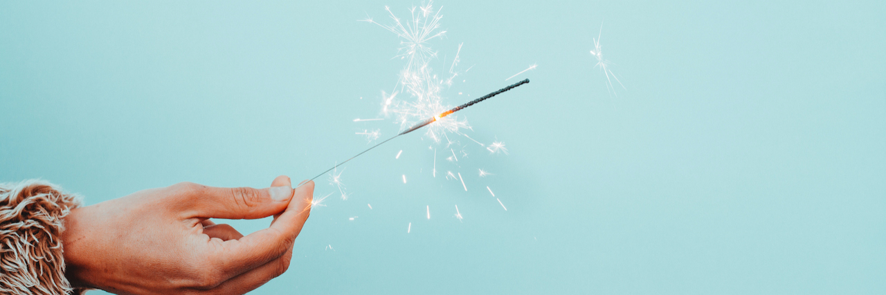 Making New Year's Mental Health 'Revelations' Instead of Resolutions A hand holding a sparkler in front of robin's egg blue background