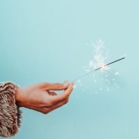 A hand holding a sparkler in front of robin's egg blue background