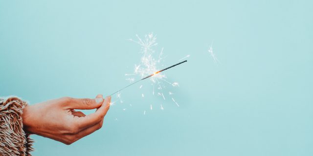 Instead of New Year's Resolutions, I'm Making New Year's Revelations A hand holding a sparkler in front of robin's egg blue background
