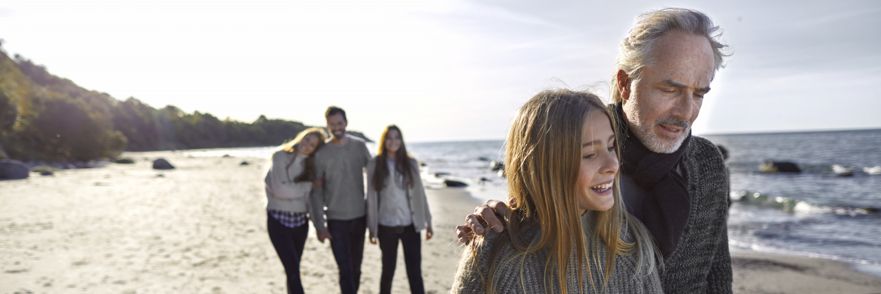 Coming to Terms With a Parent's Chronic Illness: A Child's Perspective Father and daughter strolling on the beach with family in background.