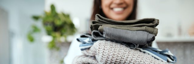 Closeup shot of a woman holding a pile of folded clothes at home