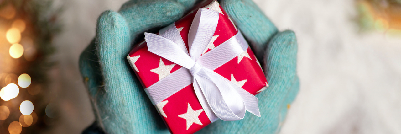 Hands in teal winter gloves holding a wrapped red present