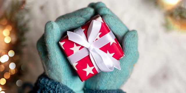 Hands in teal winter gloves holding a wrapped red present