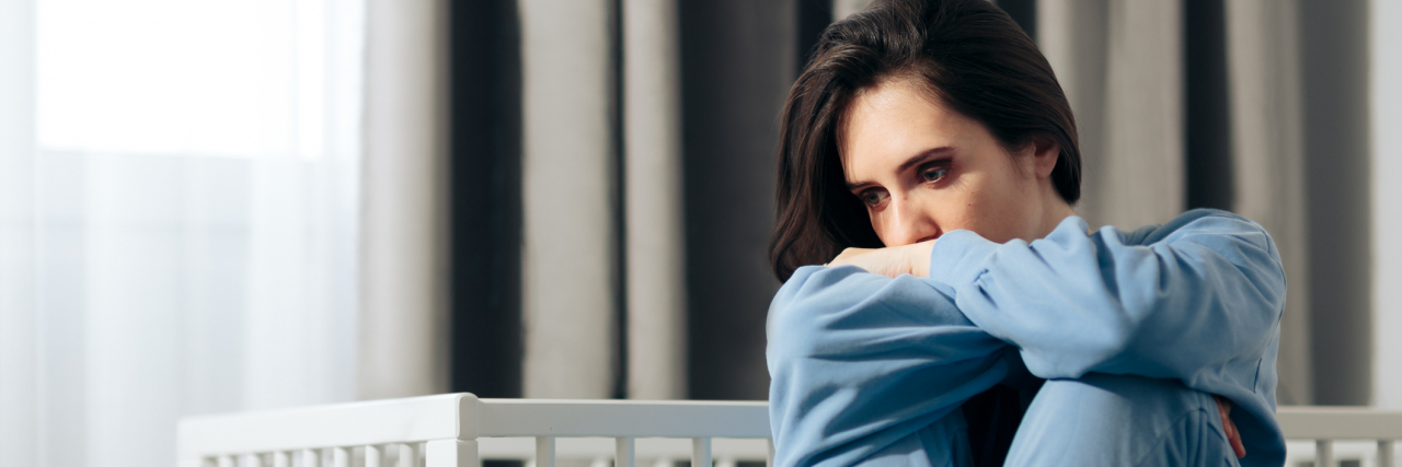 What Not to Say to a Loved One Grieving a Miscarriage Young woman sitting on a bed with her knees tucked to her chest, look away sad