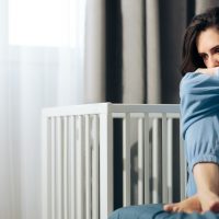 Young woman sitting on a bed with her knees tucked to her chest, look away sad