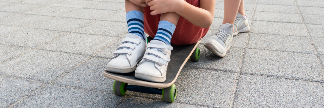 Boy wearing velcro shoes sitting on skateboard.
