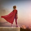 Young girl with a cape standing on a ledge overlooking the city at sunset