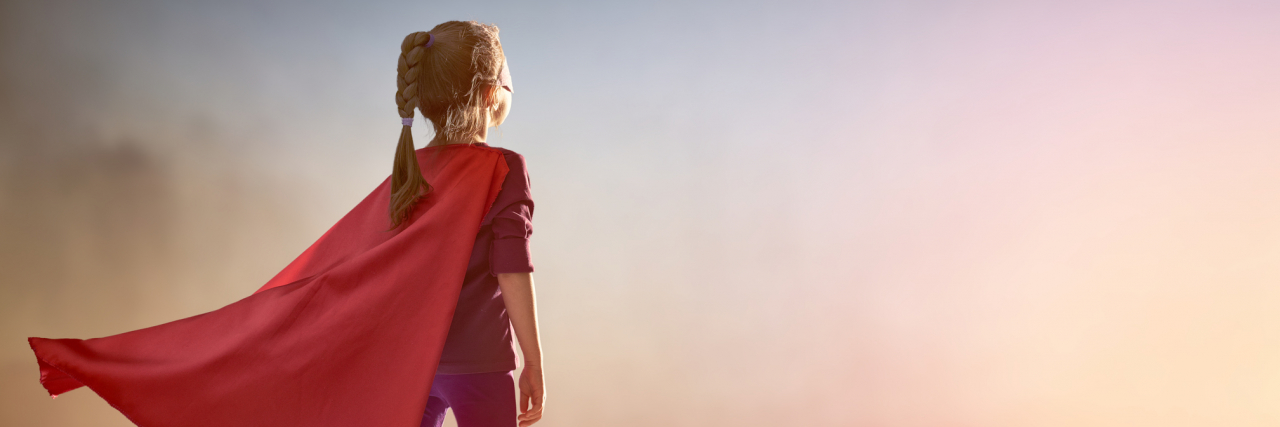 What It’s Like to Set Boundaries as a Childhood Trauma Survivor Young girl with a cape standing on a ledge overlooking the city at sunset