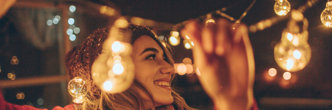 Woman wearing winter hat and scarf outside hanging up lights