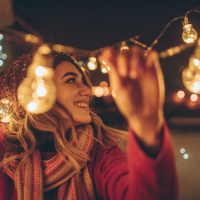 Woman wearing winter hat and scarf outside hanging up lights