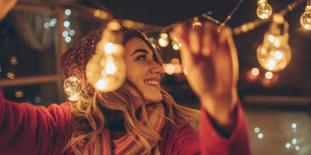 10 Mental Health Reminders for the New Year (and Beyond) Woman wearing winter hat and scarf outside hanging up lights