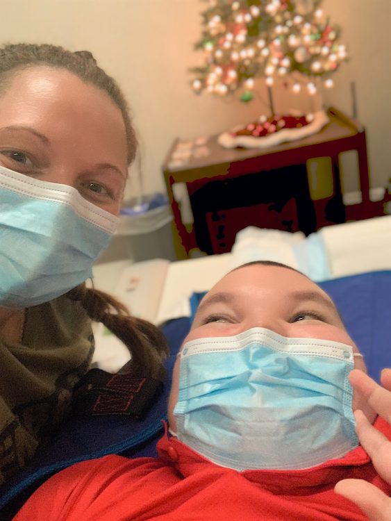 Photo of Jacob laying on exam table with his Mom next to him and Christmas tree in background