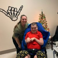 Jacob sitting in his chair with his Mom posing next to him in front of a Christmas tree
