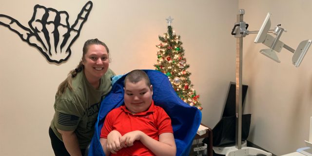 Jacob sitting in his chair with his Mom posing next to him in front of a Christmas tree