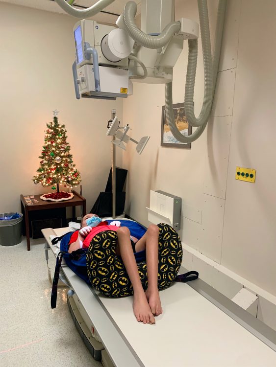 Jacoby laying on exam table with x-ray machine above him and Christmas tree behind him