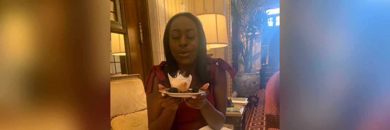 The edges of the pictures are blurred out. Centered you have a Black girl in a fabulous maroon jumpsuit with bows on the sleeves blowing out a birthday cake in a ritzy hotel in Washington DC. Her hair is straightened and next to her on the couch there's a pink mask and a camera. A pink dinner napkin sits perfectly on her lap.