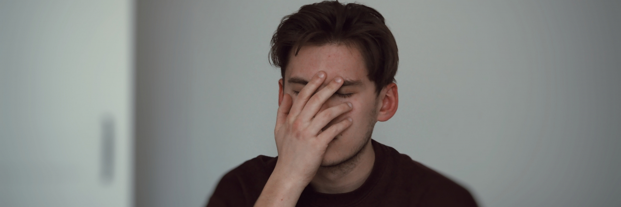 Harmful Health Phrases and Mindsets We Shouldn't Use This New Year Centered in the middle of a photograph is a white man in a red sweater with his hand over his face, clearly annoyed. He has brown hair and is against a white wall.