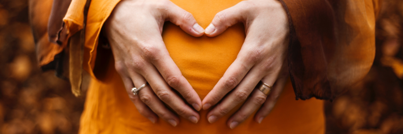 Managing Medication Risks While Pregnant with Bipolar Disorder photo of a pregnant woman holding her hands on her belly in the shape of a heart