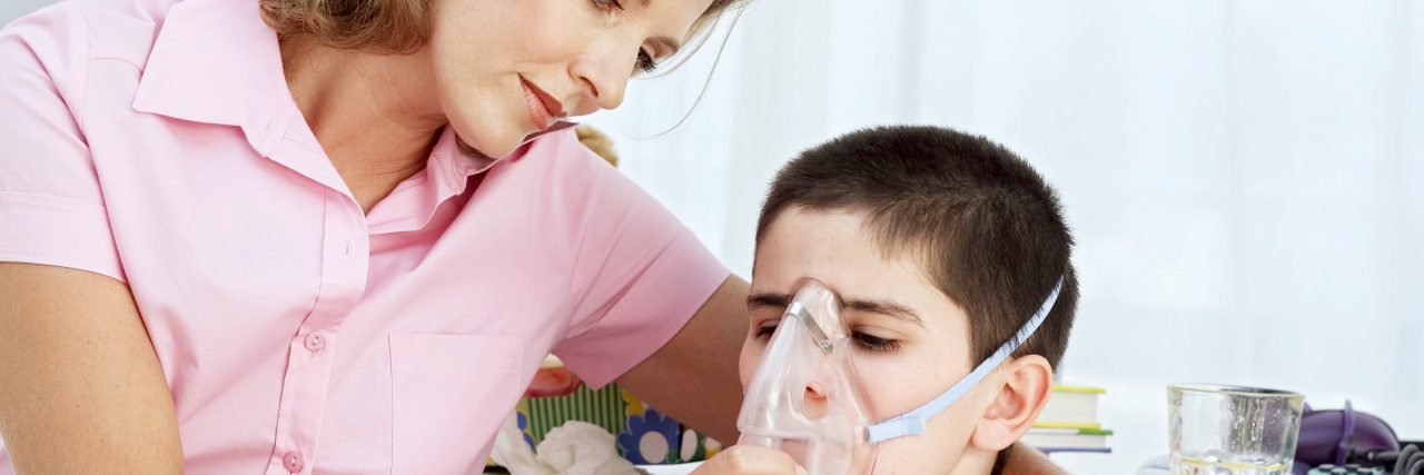 The Challenges of Coping With the Progression of Your Child's Terminal Illness  A blonde mother wearing a pink shirt hugs a brunette boy while holding an oxygen mask up to his face.