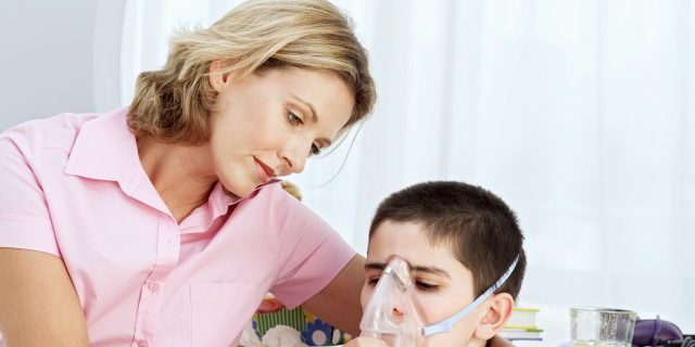 The Challenges of Coping With the Progression of Your Child's Terminal Illness  A blonde mother wearing a pink shirt hugs a brunette boy while holding an oxygen mask up to his face.