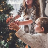 Two young children putting ornaments on a Christmas tree