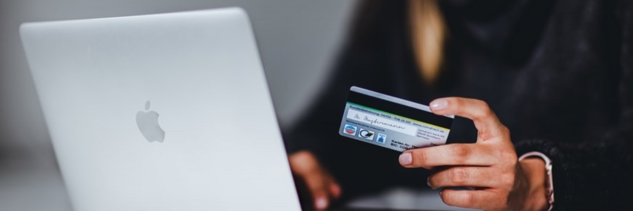 Ways to Overcome Financial Abuse in Abusive Relationships A woman wearing black holds up a credit card while sitting in front of a silver laptop.