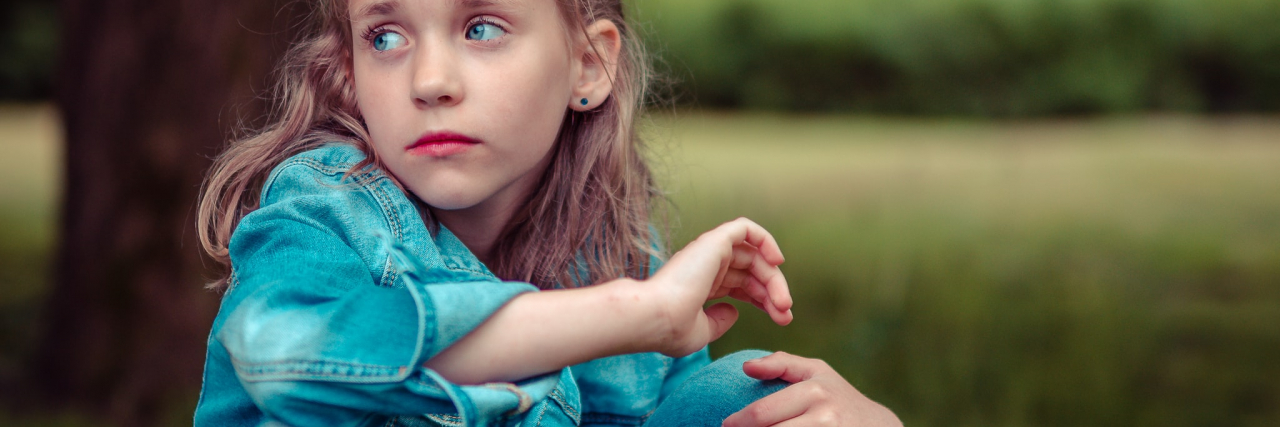 My Bullies Thought My Scars Were From Self-harm and Suicide photo of a young girl with blonde hair, sitting on grass and looking upset