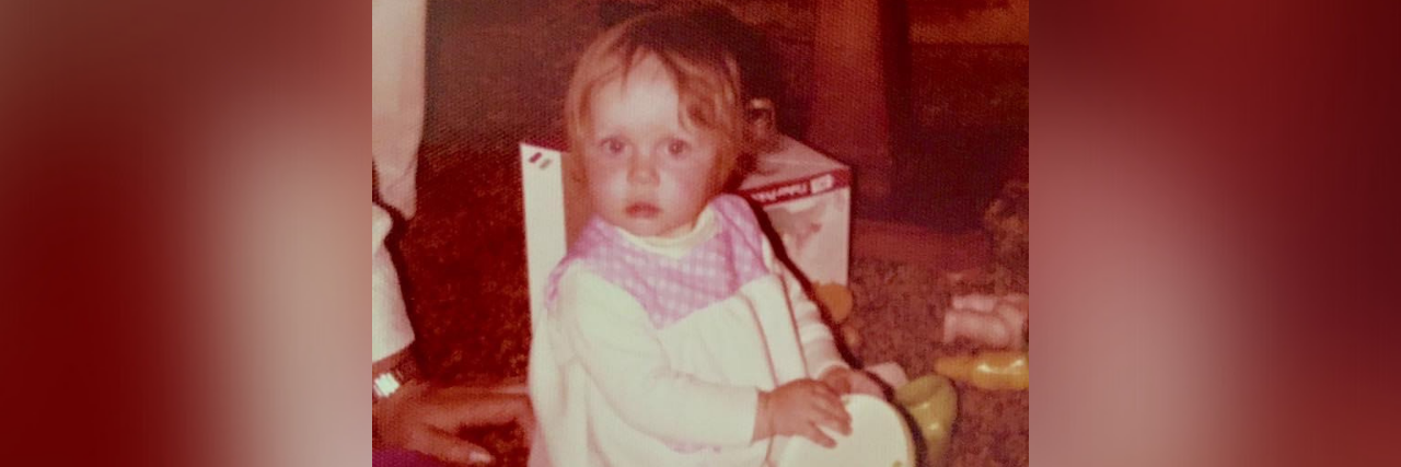 Trauma From the Responsibility to Keep a Parent Emotionally Regulated Childhood photo of contributor as young girl sitting on the floor, with a woman's hand behind her